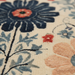 Close-up of a floral patterned textile or rug with large navy and peach flowers, blue leaves, and small red accents on an off-white background.