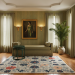 A styled interior room with a framed painting of a woman on a green wall above a beige chaise lounge, flanked by two green side tables, a large potted palm, and a floral area rug on a wood floor.