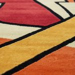 Close-up of a plush area rug with a bold geometric pattern in red, mustard yellow, orange, cream, and black.