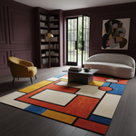 A large area rug with a bold geometric, mid-century modern design in red, blue, yellow, and cream, styled in a dark, elegant living room with a sofa, armchair, and coffee table.