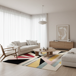 A modern living room with a large abstract geometric area rug in black, red, yellow, pink, blue, and beige, styled with a white sofa, wooden chair, round coffee table, and light wood credenza.