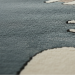 Close-up of a plush textured rug in muted blue-gray with large cream-colored abstract shapes and dark outlining.