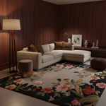 A large area rug with a dark navy floral pattern is styled in a modern living room with a cream sectional sofa, brown wood-paneled walls, and a floor lamp.