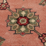 Close-up of a patterned rug with a central floral medallion in red, green, beige, and black on a dusty pink background.