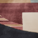 Close-up of a textured area rug with a geometric pattern, featuring a dusty rose field, a cream square, and a dark charcoal curved section.