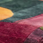 Close-up of a textured area rug with a modern abstract color-blocked pattern in deep burgundy, forest green, dusty pink, and mustard yellow.