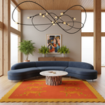 A modern living room scene featuring a curved navy blue sectional sofa, a round marble-top coffee table, a bright orange rug with yellow patterns, a wooden sideboard, potted plants, and a large black wire chandelier overhead.
