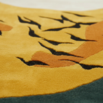 Close-up of a textured rug featuring a stylized face in mustard yellow, orange, and dark charcoal black, with a dark teal section visible at the bottom.
