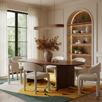 A modern dining room set featuring a dark wood oval table and six light beige upholstered chairs, arranged on a yellow and green patterned rug. The room has warm cream walls, a built-in illuminated shelving unit, and a large window with sheer curtains.