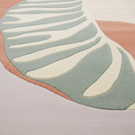 Abstract area rug with a modern organic pattern featuring sage green, cream, dusty pink, and pale lavender sections.