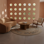 A styled interior scene with a curved tan sofa, a mid-century armchair, a round wooden coffee table, and a circular woven rug in a warm neutral room. A terracotta wall features multiple circular cutouts showing greenery outside.