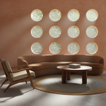 A modern living room scene with a curved brown leather sofa, a matching mid-century wooden armchair, a round coffee table, and a large woven area rug. The wall behind features a grid of circular frosted windows looking out onto greenery.