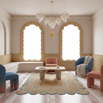 A beautifully styled bohemian living room featuring a central round coffee table on a patterned rug, surrounded by pink and blue armchairs. The room has two large arched windows with scalloped gold frames, a built-in bench, and a modern glass chandelier.
