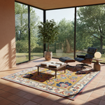 A large traditional oriental area rug in mustard yellow and cream with blue, red, and brown floral patterns, styled in a modern mid-century modern living room with a wooden coffee table, lounge chair, and ottoman.