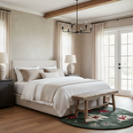A styled bedroom interior featuring a bed dressed in white and beige linens, flanked by dark wood nightstands with table lamps. A rustic wooden bench sits at the foot of the bed on a green patterned rug, with beige walls, sheer curtains, a black chandelier, and glass French doors in the background.