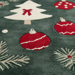 Close-up of a dark green textured rug with a festive Christmas pattern featuring red ornaments, a white Christmas tree with a red bow, and white pine branches.