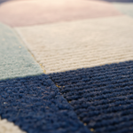 Close-up of a textured patchwork rug with geometric color blocks in navy blue, cream, light blue, and pale pink, showing the detailed pile and weave.