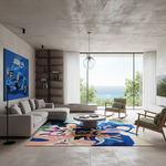 A modern living room with a large abstract multicolor area rug, a light gray sectional sofa, a round coffee table, and two wooden chairs. The room features a concrete ceiling, white curtains, and a large window overlooking the ocean. A blue car artwork hangs on the wall.