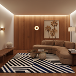 A modern living room featuring a curved taupe sectional sofa, a bold black and white striped area rug, a glass-top coffee table with stone bases, and a warm wood-paneled wall with a palm tree artwork.