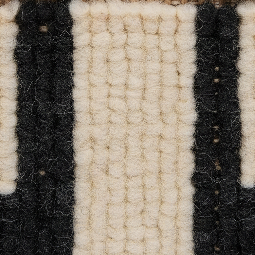 Close-up of a textured woven rug or textile with alternating thick vertical stripes in off-white/cream and black.