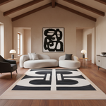 A modern living room with a large black and off-white geometric area rug on a wood floor, featuring a curved white sofa, a black armchair, and a framed abstract black-and-white wall art piece.