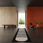 A long rectangular area rug with a black border, black and white striped pattern, and a cream-colored rounded bottom section, displayed in a modern minimalist interior hallway with wood-paneled walls.