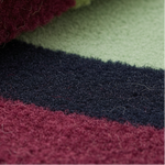 Rolled corner of the Maia Burgundy Geometric rug showing burgundy, navy, and sage striped bands