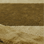Close-up of a plush shag rug in warm brown with a contrasting beige ribbed border, showing the soft texture and pile direction.
