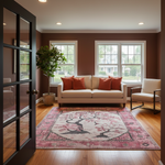A styled living room interior featuring a large rectangular area rug with a pink and beige cherry blossom tree pattern, placed on a hardwood floor in front of a cream sofa with orange accent pillows.
