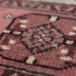 Close-up of a woven rug with a dusty rose and burgundy base, featuring a central medallion pattern in black and cream.