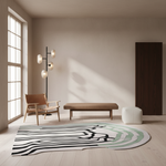 A modern living room scene with a large abstract area rug on the floor, featuring black, white, and soft green wavy lines. The room includes a wooden armchair, a floor lamp, a low bench, a white pouf, and a tall dark wood door, all set against warm beige walls and light wood flooring.