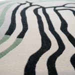 A close-up of a textured area rug featuring a modern abstract pattern of thick black wavy lines on an off-white background, with light sage green accents.
