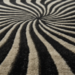 A close-up of a textured area rug featuring a black and cream spiral or zebra-like stripe pattern radiating from the center.