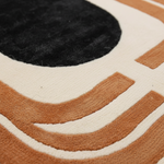 Close-up of a plush area rug with a modern abstract design featuring a black oval and wavy tan and cream stripes.