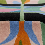 Close-up of a colorful area rug with a retro abstract pattern in shades of pink, blue, green, orange, and black.