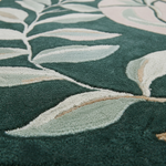 Close-up of a plush area rug with a raised botanical leaf pattern in dark green, pale sage, cream, and soft blush tones.