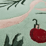 Close-up of a textured rug with a mint green background, a light pink curved stripe, dark green leafy accents, and a red ornament motif.