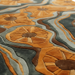Close-up of a textured area rug with a 3D floral and wavy organic pattern in warm orange, mustard, brown, and slate blue-gray.