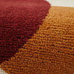Close-up of a textured, loop-pile rug with a diagonal color-block design in deep burgundy red and warm mustard orange.