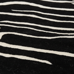 A close-up of a black and white zebra-patterned textile, showing the texture of the wool or felt material with wavy white stripes on a black background.