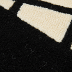 Close-up of a textured rug with a bold black and cream geometric pattern, showing the detailed loop pile texture.