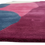 Close-up of a plush area rug with an abstract wavy pattern in magenta, dusty blue, and cream, showing the soft pile texture.