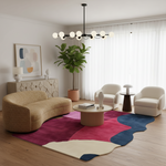 A modern living room featuring a bold abstract area rug in pink, navy, and cream, styled with a curved beige sofa, two cream armchairs, a round coffee table, and a large potted plant.