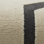 Close-up of a textured area rug with a cream-colored field and a bold dark charcoal gray geometric border.