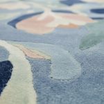 Close-up of a plush area rug with a soft, abstract floral pattern in shades of light blue, navy, pale pink, and mint green.