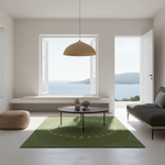 A modern living room with a green area rug featuring a gold circular sunburst pattern, styled with a round wooden coffee table, a woven pendant light, and a gray sofa, overlooking a scenic ocean view.