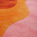 Close-up of a plush textured rug with abstract wavy color-blocked sections in orange, pink, and a small portion of orange-red.