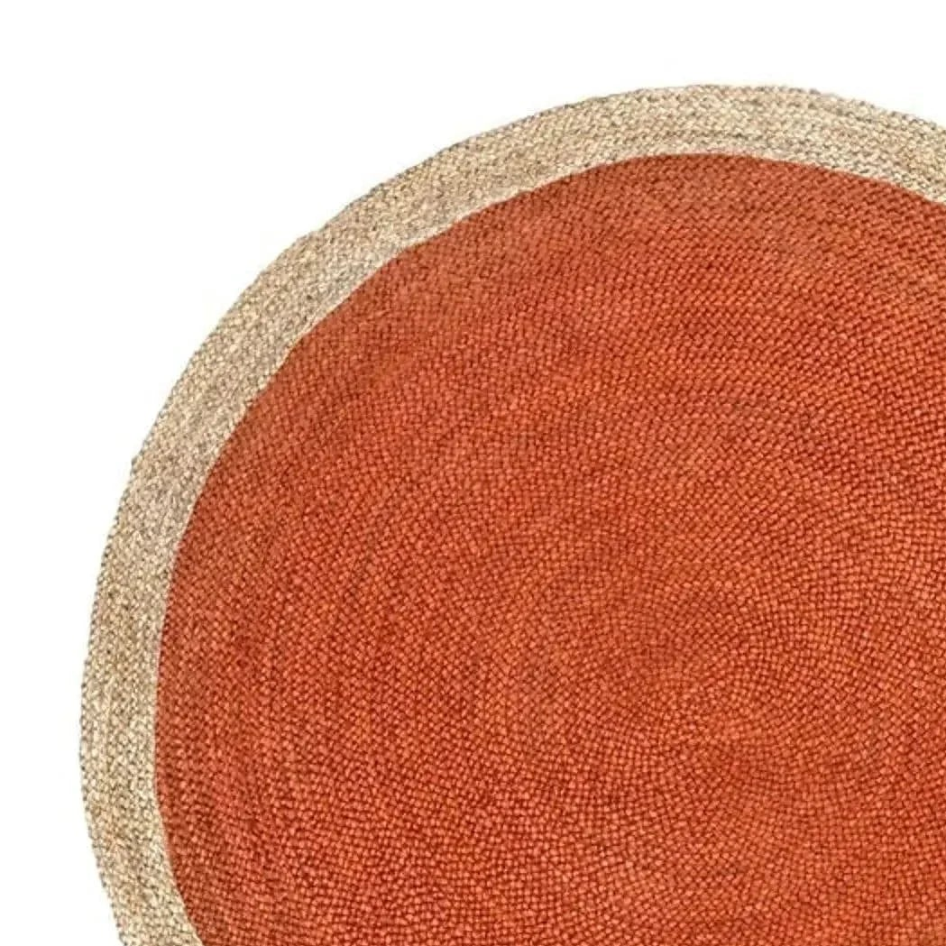 A close-up of a round woven rug with a warm rust-orange center and a natural beige braided border on a white background.
