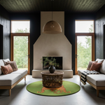 A styled living room interior featuring a round green rug with a tiger design in the center, surrounded by a round wicker coffee table, two white sofas with patterned pillows, and a large beige fireplace with tall windows looking out to green trees.