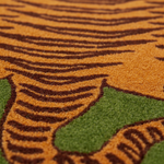 Close-up of a textured rug with a stylized animal pattern in orange, dark brown, and green, showing the detailed pile texture.